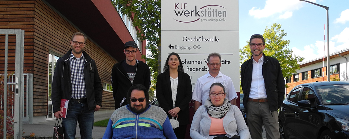 Gruppenfoto der Schichtwechselteilnehmer vor dem Schild der St. Johannes Werkstätte.