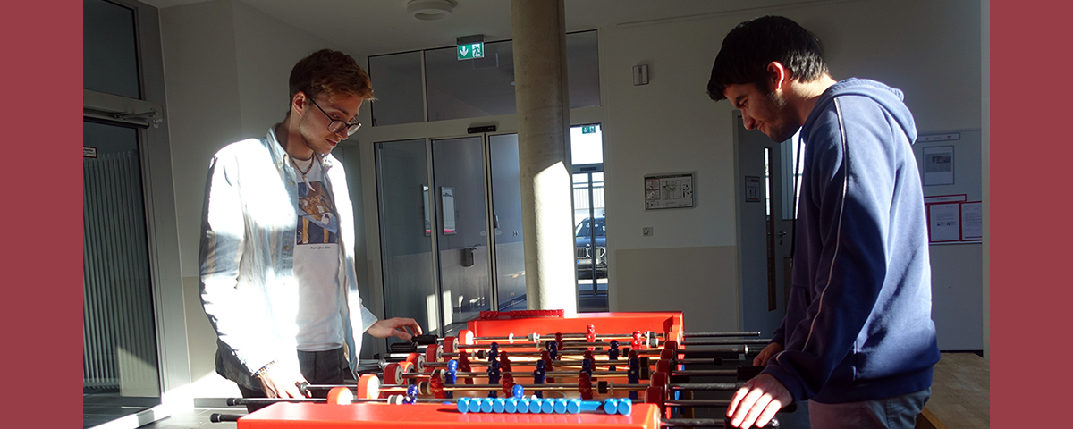 Felix und Ali stehen an einem Kicker und spielen gegeneinander.