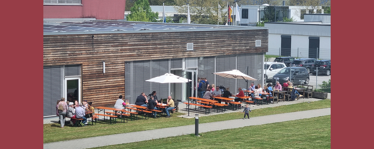 Menschen sitzen auf Bierbänken auf der Terrasse der St. Johannes Werkstätte.