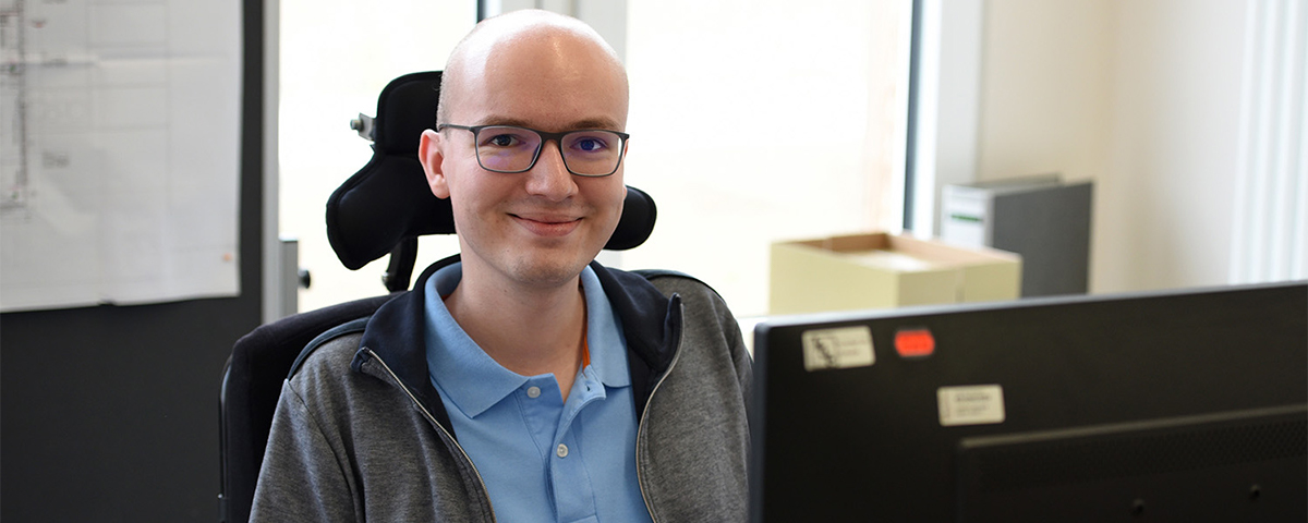 Matthias Schießl sitzt an einem Tisch. Vor ihm stehen ein Bildschirm, Maus und Tastatur.