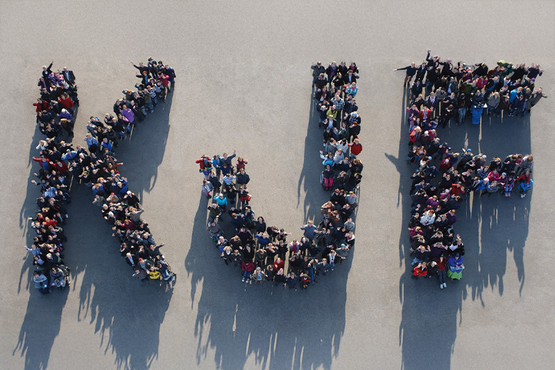 Luftaufnahme von Mitarbeitern der KJF-Werkstätten, die die Form der Buchstaben K J und F nachstellen.