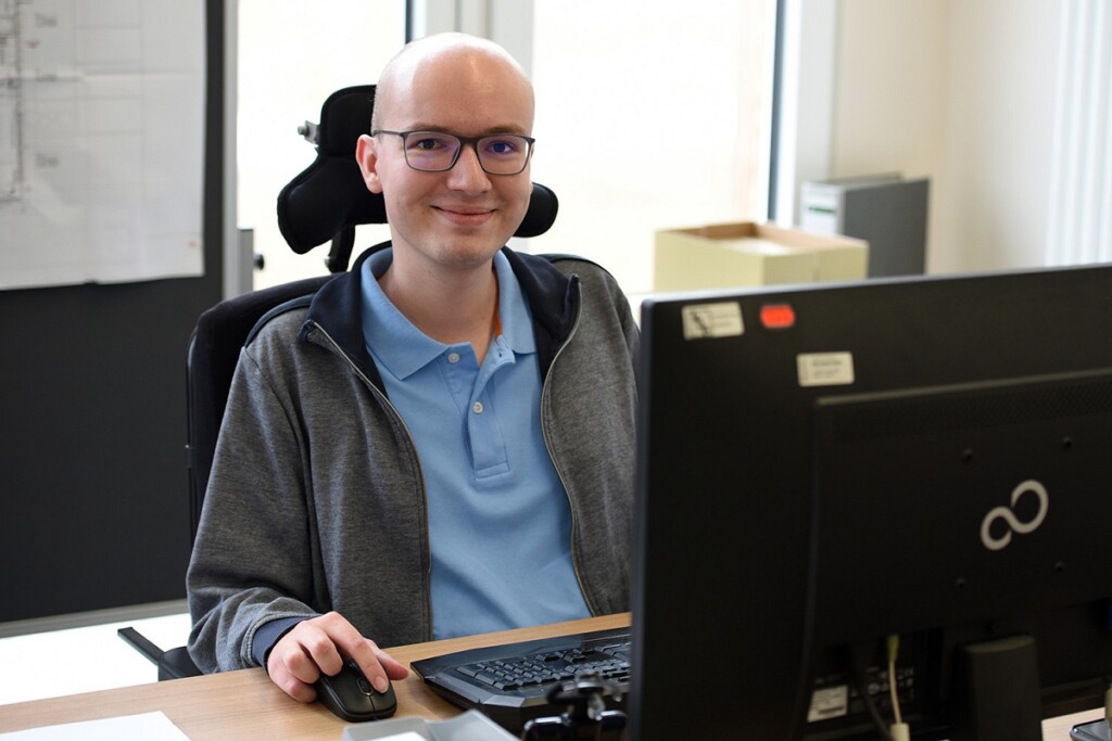 Matthias Schießl sitzt an einem Tisch. Vor ihm stehen ein Bildschirm, Maus und Tastatur.