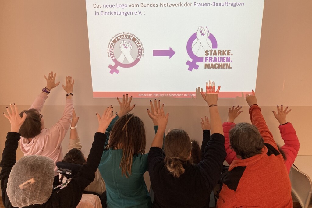 Frauen strecken Hände mit lila Fingernägeln Richtung neues Logo der Frauenbeauftragten BAG
