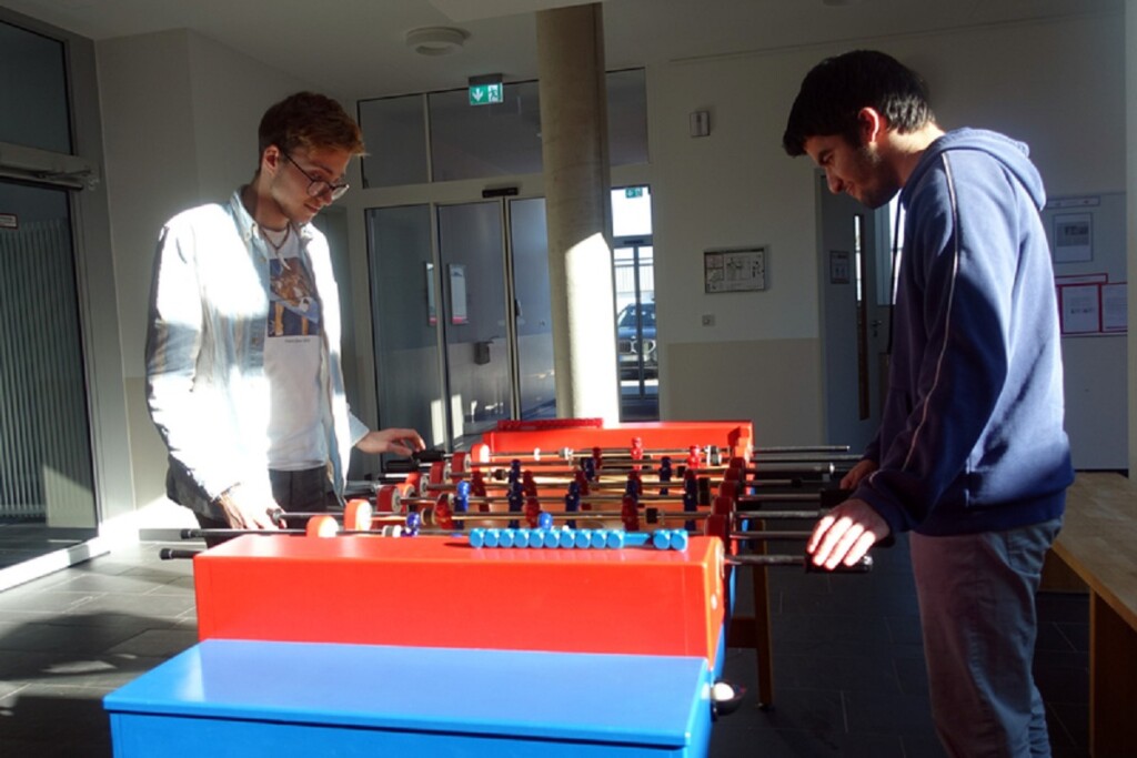 Felix und Ali stehen an einem Kicker und spielen gegeneinander.