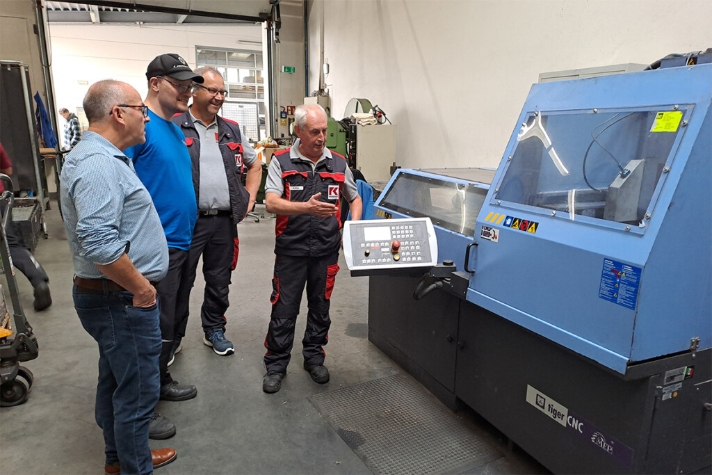 Die Teilnehmer stehen an einer großen Maschine in der Werkstätte.