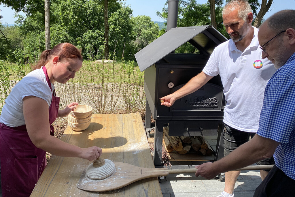 Drei Mitarbeiter bereiten Brot vor, das in den hauseigenen Ofen geschoben wird.