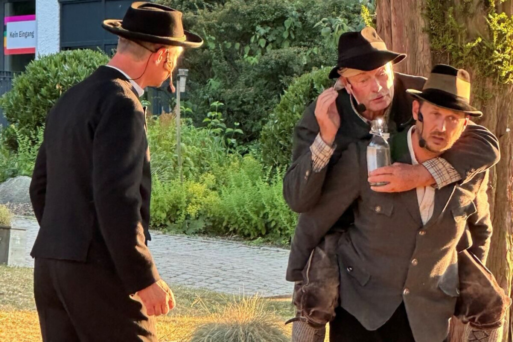 Szene aus dem Theaterstück Der Brandner Kaspar und das ewig Leben. Ein Schauspieler trägt den anderen Huckepack.