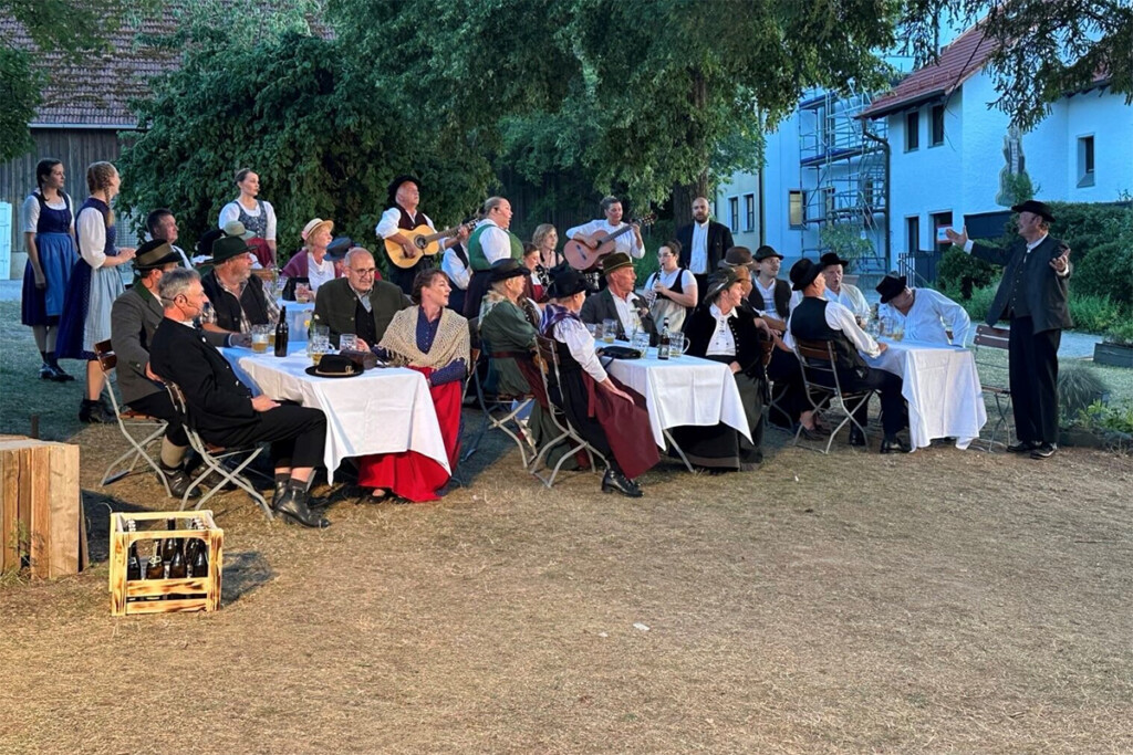 Die Schauspieler sitzen an Tischen und singen gemeinsam.
