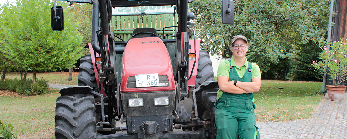 Sabrina Kiesl steht neben einen Traktor und schaut in die Kamera