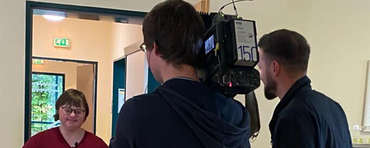 Mitarbeiterin schiebt Servierwagen. Ein Filmteam filmt sie dabei.