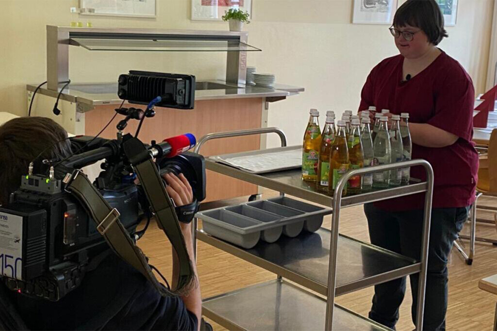 Kameramann kniet vor Mitarbeiterin mit Servierwagen
