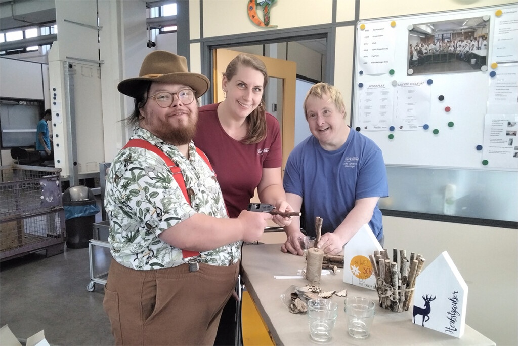 Mitarbeiter stehen gemeinsam am Arbeitstisch und blicken stolz in die Kamera