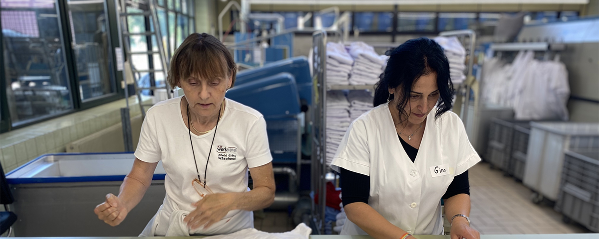 Feride Niedermeier faltet Wäsche in der Wäscherei der Bruder Konrad Werkstätte. Werkstatträtin Erika Stelzl unterstützt sie dabei.