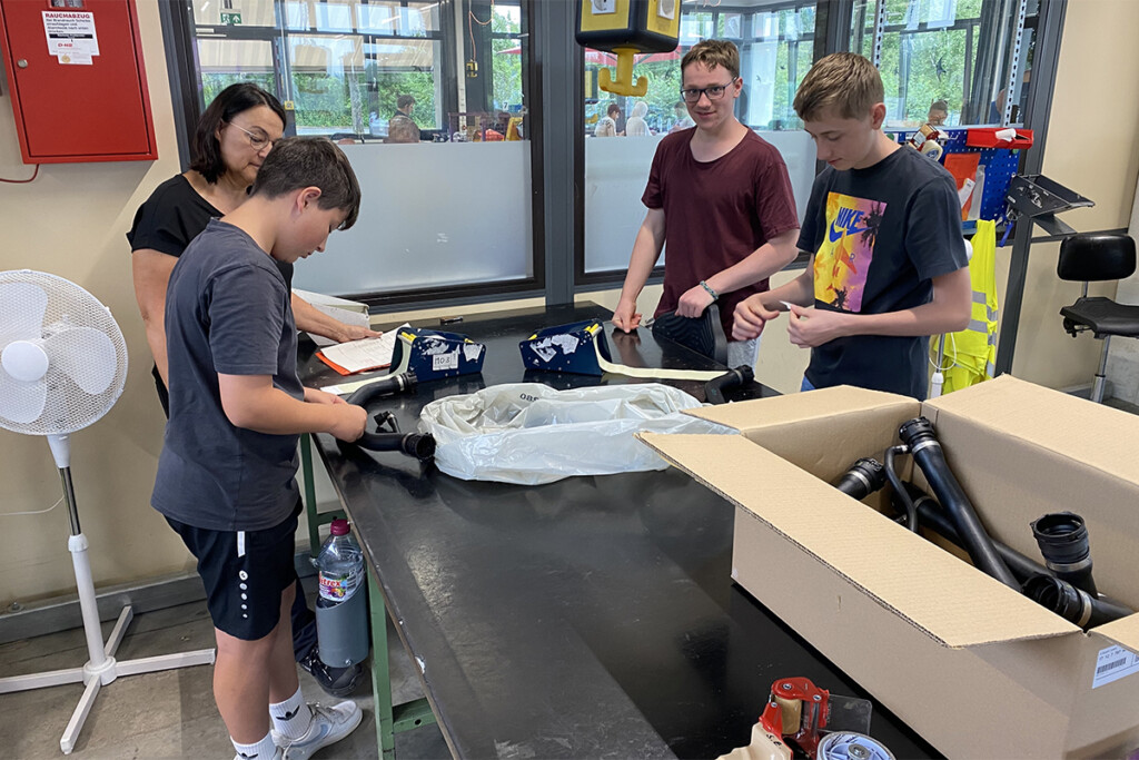 Drei Schüler verpacken Schläuche in der Abteilung Montage der Bruder Konrad Werkstätte. Ingrid Zipperer erklärt ihnen dabei die Arbeitsabläufe.