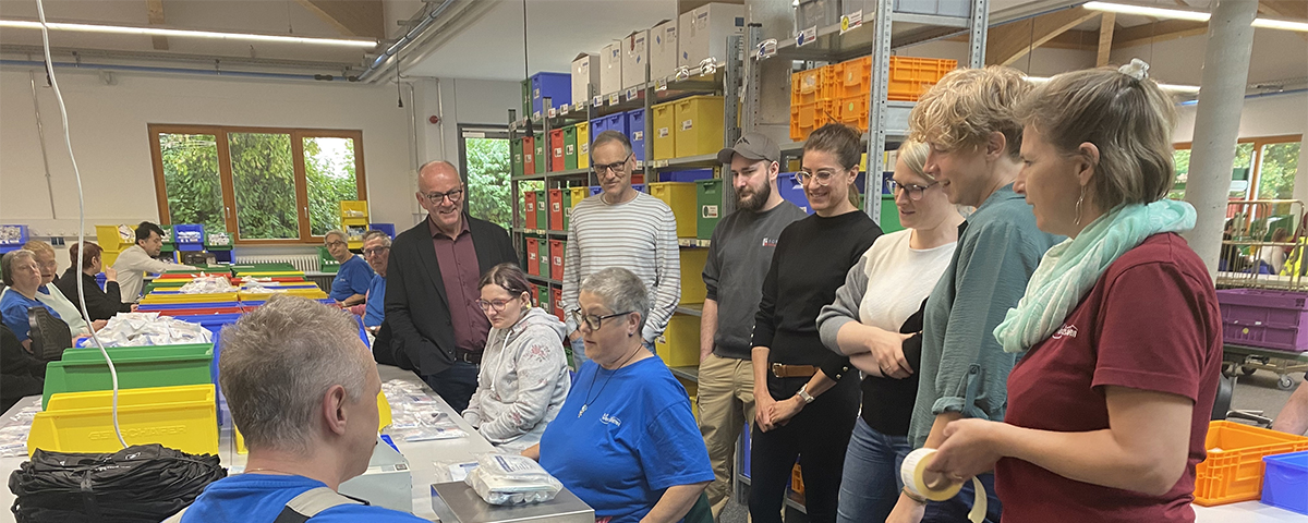 Mitarbeiter der Werkstättte und die Teilnehmer der Aktion Schichtwechsel unterhalten sich in der Montageabteilung.