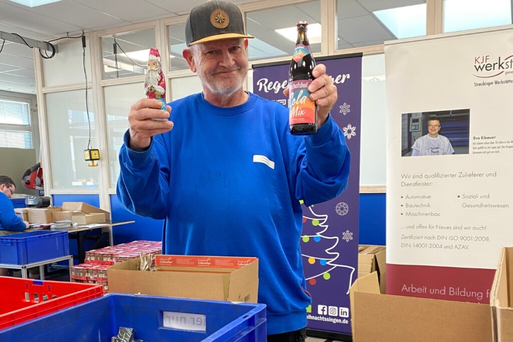 Ein Mitarbeiter grinst in die Kamera und hebt ein Schokonikolaus hoch in einer Hand und in der anderen Hand hebt er eine Spezi hoch