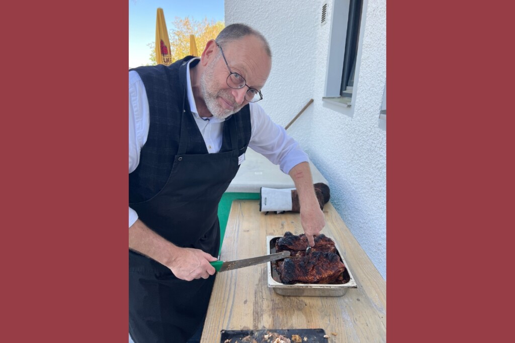 Eine Person schneidet im Freien einen knusprig gebratenen Schweinebraten auf einem Holztisch an.
