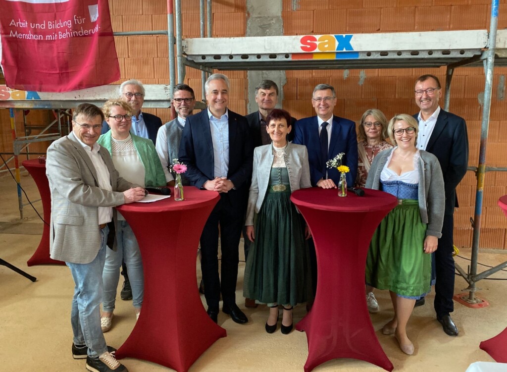 Mehrere Personen stehen für ein Gruppenfoto im Rohbau vor einem Baugerüst und einer Fahne der KJF Werkstätten.