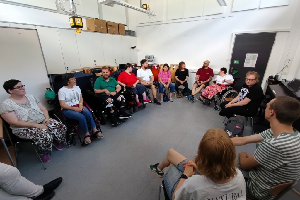 Mehrere Personen sitzen in einem Stuhlkreis in einem Seminarraum der OTH Regensburg. Darunter sind Rollstuhlnutzende sowie Studierende. Die Gruppe befindet sich in einem gemeinsamen Austauschgespräch.