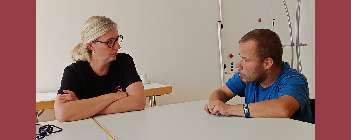 Silke Prößl unterhält sich mit einem Mitarbeiter der Werkstätten an einem Tisch.
