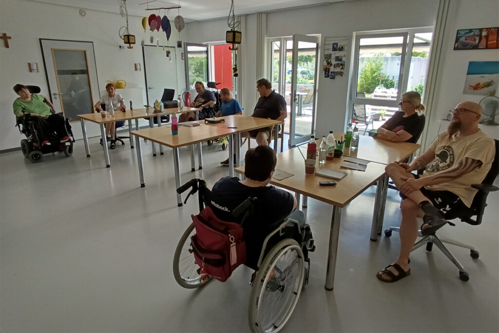 Silke Prößl sitzt zusammen mit der Prüfgruppe "einfach g'macht" im Gruppenraum und sprechen miteinander.