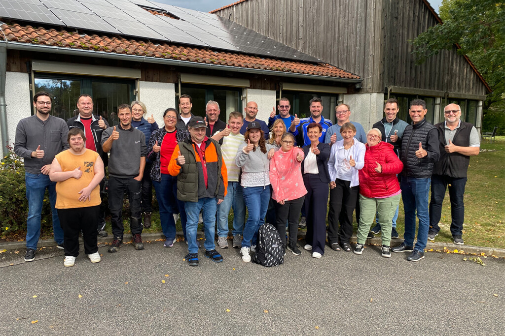 Gruppenfoto der Schichtwechsler. 23 Personen stehen in zwei Reihen vor einem Gebäude mit Solardach und blicken in die Kamera. Die meisten lächeln und zeigen einen Daumen nach oben.
