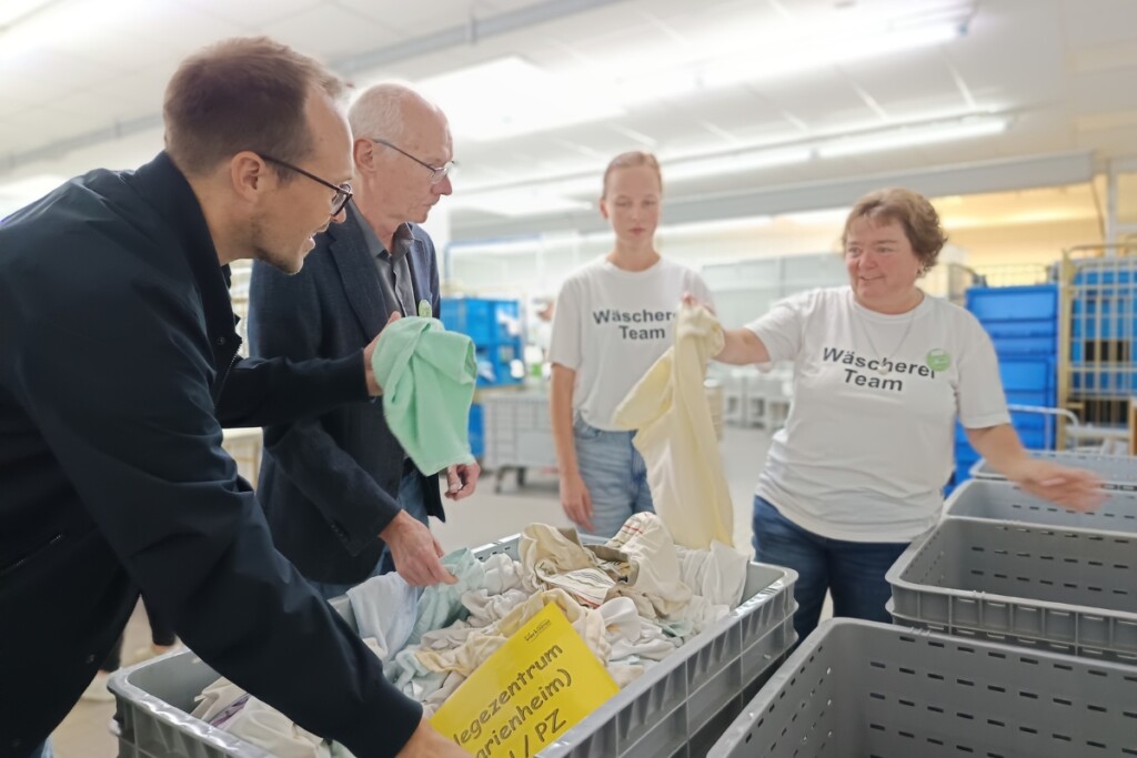 Gäste des Aktionstags „Schichtwechsel“ arbeiten gemeinsam mit Beschäftigten in der Wäscherei. Dabei sortieren sie Wäsche und tauschen sich über die Arbeitsabläufe aus.
